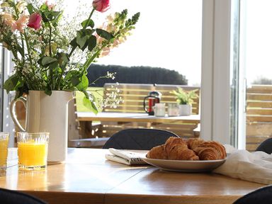 A dining table with a vase of flowers croissants and glasses of orange juice near large windows at Ash Cottage in Lucker near Warenford
