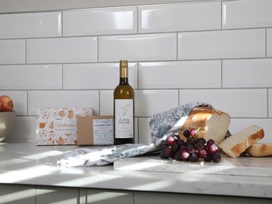 A kitchen countertop with a loaf of bread grapes a bottle of white wine and welcome packs at Ash Cottage in Lucker near Warenford