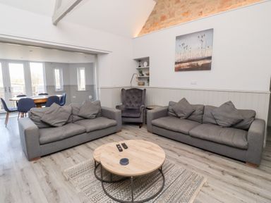 A living room with two gray sofas a round wooden coffee table and an armchair at Ash Cottage in Lucker near Warenford
