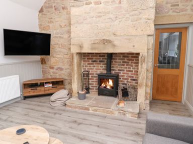 A living room with a wood burning stove in a stone fireplace a wall mounted television and a wooden cabinet at Ash Cottage in Lucker near Warenford