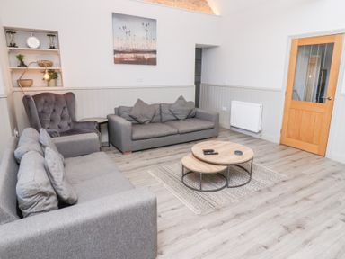 A living room with two grey sofas a grey armchair wooden coffee tables on a rug and a wooden door at Ash Cottage in Lucker near Warenford