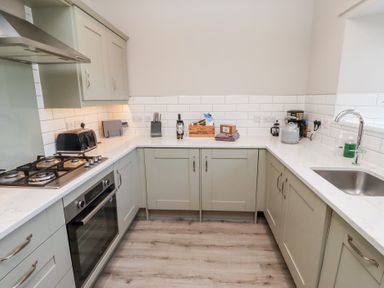 A kitchen with green cabinets a gas stove an oven a sink and various kitchen appliances on the countertop at Ash Cottage in Lucker near Warenford