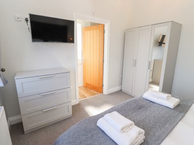 A bedroom with a bed with folded towels a wardrobe a chest of drawers a wall-mounted TV and an open door at Ash Cottage in Lucker near Warenford