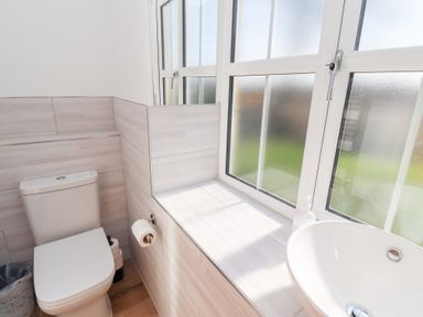 A bathroom with a toilet a sink a frosted window and a toilet paper holder at Ash Cottage in Lucker near Warenford