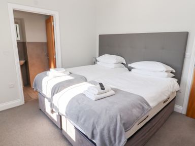A bedroom with two single beds pushed together each with white bedding grey throws and pillows a remote on towels on the beds a door leading to a bathroom at Ash Cottage in Lucker near Warenford
