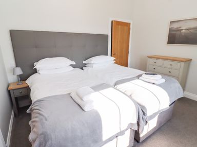 A bedroom with two single beds with gray headboards and white linens at Ash Cottage in Lucker near Warenford