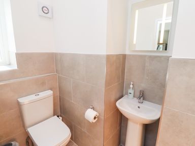 A bathroom with a toilet a pedestal sink a wall mirror and a window at Ash Cottage in Lucker near Warenford