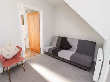 A small room with a striped gray and black sofa and a pink chair with a cushion near a wooden door at Ash Cottage in Lucker near Warenford