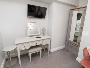A room with a white dressing table and stool under a wall-mounted television and a mirrored wardrobe in the corner at Ash Cottage in Lucker near Warenford