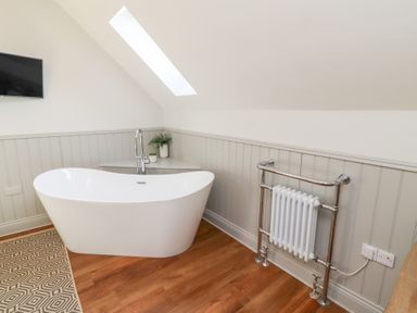 A bathroom with a freestanding bathtub a wall-mounted television and a towel radiator at Ash Cottage in Lucker near Warenford