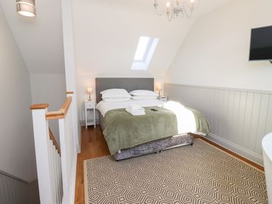 A bedroom with a double bed green blanket bedside tables lamps skylight and patterned rug at Ash Cottage in Lucker near Warenford
