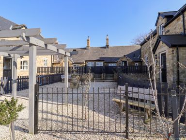An outdoor courtyard with stone buildings wooden pergola benches and gravel at Ash Cottage in Lucker near Warenford