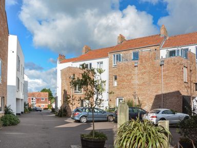 A street view with brick and white buildings parked cars and plants in pots at Skylark in Southwold