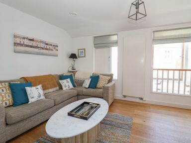 A living room with a sectional sofa blue and patterned cushions a marble oval coffee table and two windows at Skylark in Southwold