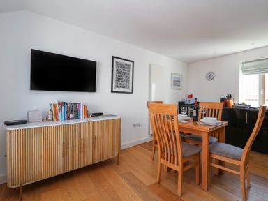 A dining area with wooden table and chairs a cabinet with books and a wall mounted TV at Skylark in Southwold