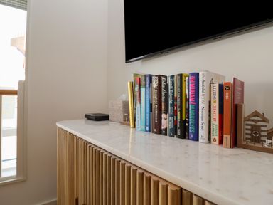 A white marble countertop with a row of books a tissue box a remote and a small wooden house decoration at Skylark in Southwold
