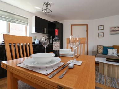 A dining table set with plates bowls cutlery wine glasses and a bottle of wine in a kitchen and living area at Skylark in Southwold