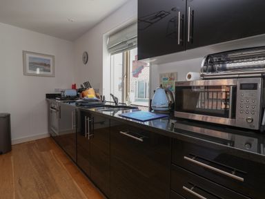 A kitchen with black cabinets a microwave a toaster a kettle a sink and a window at Skylark in Southwold