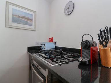 A kitchen countertop with a gas stove a blue toaster a red coffee machine a knife block with scissors and knives a wall clock and a framed picture at Skylark in Southwold