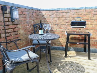 An outdoor area with a table, chairs, wine, and a grill at Skylark in Southwold