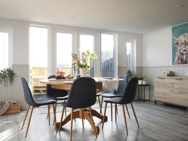 A dining area with a round wooden table and six dark chairs at Elm Cottage in Lucker near Warenford