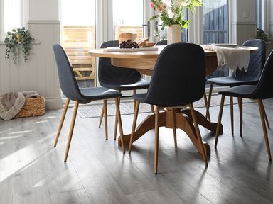A dining area with a wooden round table and six gray chairs near glass doors with plants and a basket on the floor at Elm Cottage in Lucker near Warenford