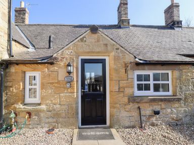 Stone cottage exterior with black door and white framed windows at Elm Cottage in Lucker near Warenford