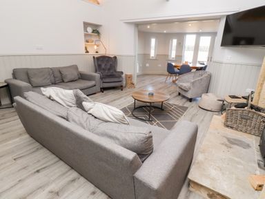 A living room with gray sofas armchairs a round wooden coffee table and a dining area in the background at Elm Cottage in Lucker near Warenford