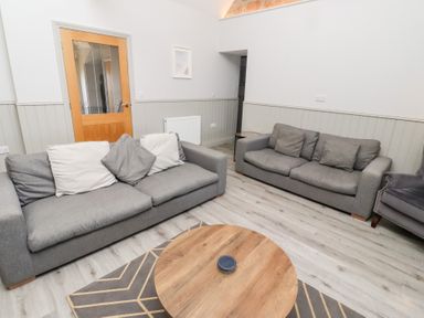 A living room with two grey sofas a wooden round coffee table and a grey armchair at Elm Cottage in Lucker near Warenford