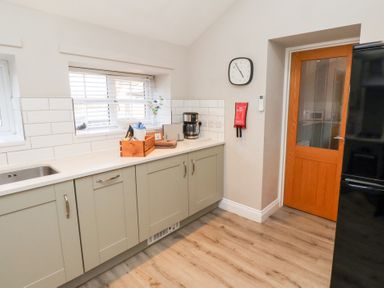 A kitchen with cabinets a coffee maker a clock on the wall and a wooden door at Elm Cottage in Lucker near Warenford