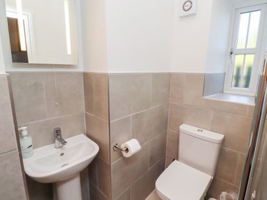 A bathroom with a white sink and soap dispenser a toilet with a roll of toilet paper on the wall and a window at Elm Cottage in Lucker near Warenford