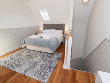 A bedroom with a double bed bedside tables lamps and a patterned rug at Elm Cottage in Lucker near Warenford