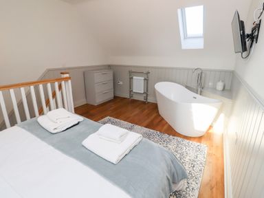 A bedroom with a bed folded towels freestanding bathtub small dresser and wall-mounted television at Elm Cottage Lucker near Warenford
