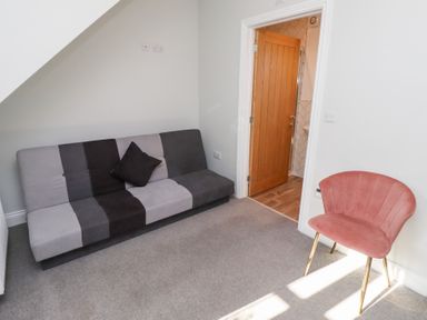 A room with a gray and black striped sofa and a pink chair near a wooden door at Elm Cottage in Lucker near Warenford