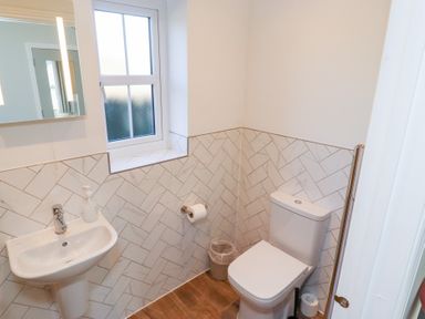 A small bathroom with a toilet sink mirror window and trash bin at Elm Cottage in Lucker near Warenford
