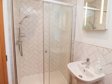 A bathroom with a glass-enclosed shower, a handheld showerhead, a white sink with a faucet, and a soap dispenser at Elm Cottage Lucker near Warenford
