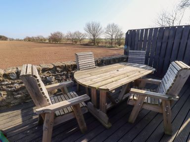 A wooden outdoor table with four wooden chairs on a deck overlooking a field at Elm Cottage in Lucker near Warenford