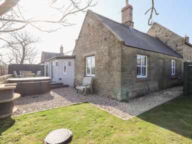 An outdoor area with a stone building patio furniture hot tub and gravel ground at Elm Cottage in Lucker near Warenford