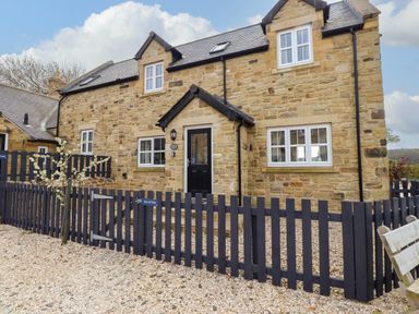 Stone house with black door and windows surrounded by black picket fencing and gravel at Oak Cottage in Lucker near Warenford