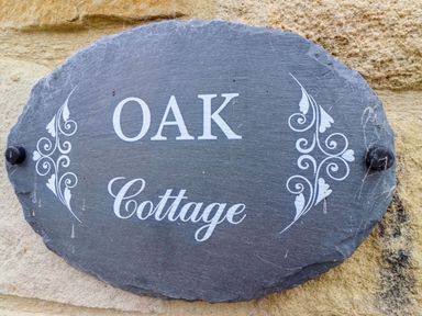 A stone sign with the text Oak Cottage mounted on a rough stone wall at Oak Cottage in Lucker near Warenford
