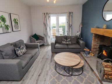 A living room with two grey sofas a round wooden coffee table a fireplace and glass doors leading outside at Oak Cottage in Lucker near Warenford