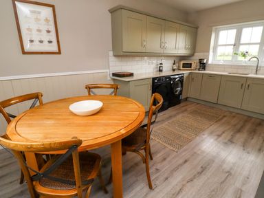A kitchen with wooden table and chairs near grey cabinets and window at Oak Cottage in Lucker near Warenford