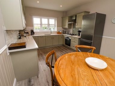 A kitchen with a round wooden table and chairs a refrigerator an oven a gas stove and cabinets at Oak Cottage in Lucker near Warenford