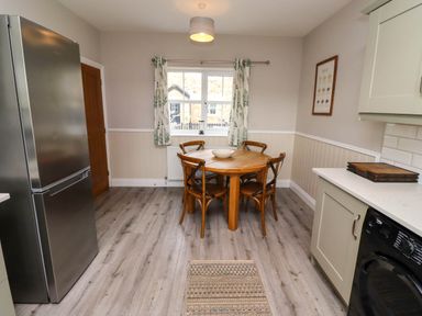 A kitchen with a wooden round table and four chairs a refrigerator and washing machine at Oak Cottage in Lucker near Warenford