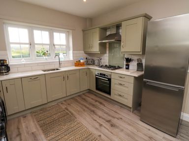 A kitchen with cabinets a stainless steel refrigerator a stove a sink and a window with flowers on the sill at Oak Cottage in Lucker near Warenford