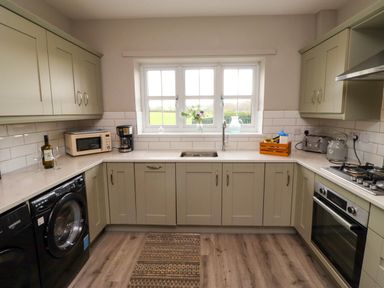 A kitchen with cabinets countertop washing machine oven and window at Oak Cottage Lucker near Warenford