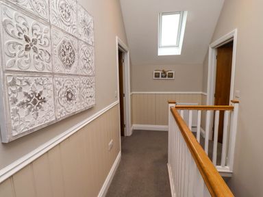 A hallway with wooden handrails wall paneling decorative wall art and a skylight at Oak Cottage in Lucker near Warenford