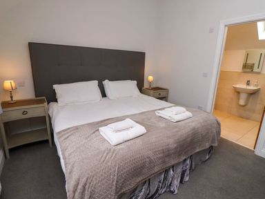 A bedroom with a bed and bedside tables with lamps next to an ensuite bathroom at Oak Cottage in Lucker near Warenford