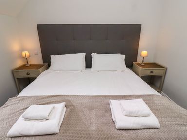 A bedroom with a double bed with white linens and pillows two bedside tables with lamps and folded towels on a blanket at Oak Cottage in Lucker near Warenford