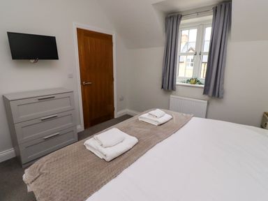 A bedroom with a bed covered with blankets and towels a chest of drawers a wall-mounted television and a window with curtains at Oak Cottage in Lucker near Warenford